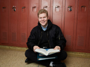 Picture of Pathways alum Noah sitting on floor in front of lockers