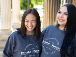 Two female alumna standing side-by-side laughing