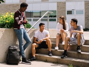 Four teenage students sitting on steps in front of a school