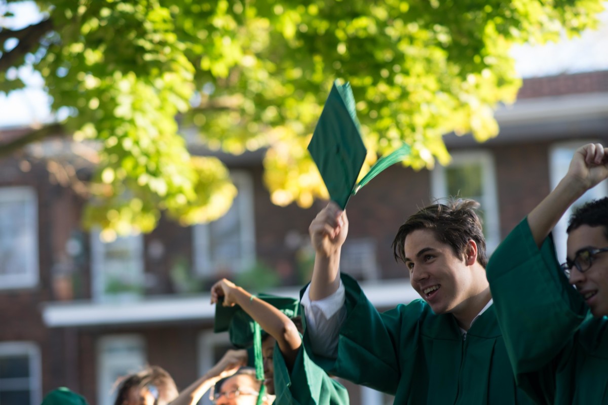 Student outdoors, wearing graduation robes and cap, looking into the distance