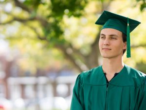 Student outdoors, wearing graduation robes and cap, looking into the distance